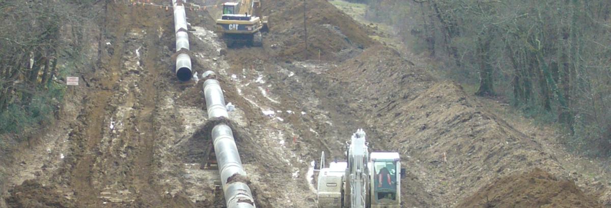 Photo prise sur un chantier d’installation d’une canalisation de transport de matière dangereuse. Une pelleteuse est en train de creuser une tranchée pour un tuyau de très gros diamètre.